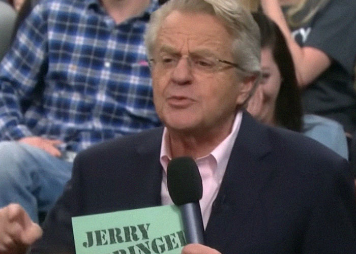 TV show host holding a cue card, addressing the audience during a reality TV show episode.