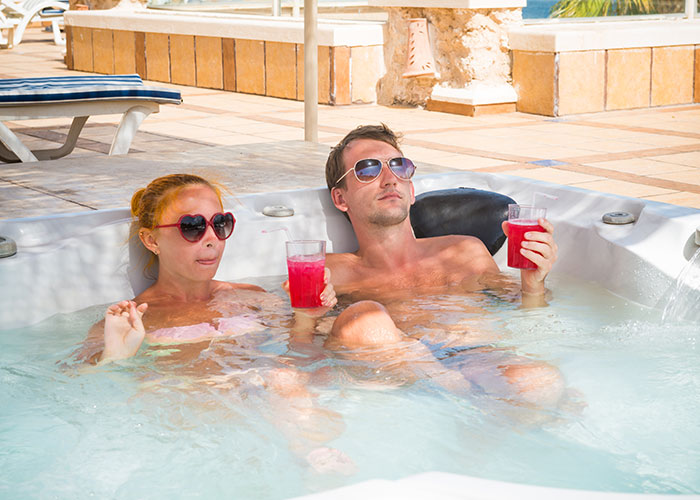 Couple relaxing in a hot tub with drinks, reflecting on reality TV show secrets revealed by insiders.