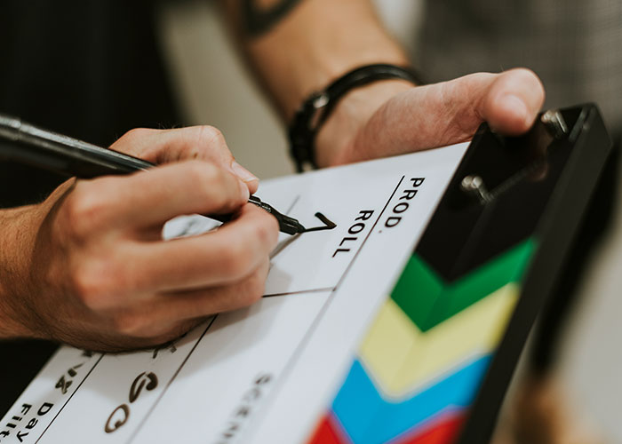 Person writing on clapperboard, representing behind-the-scenes of reality TV shows.