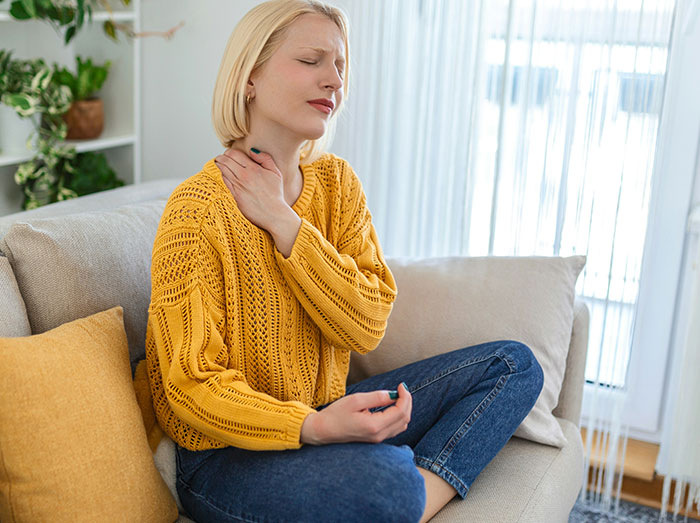 Woman in yellow sweater sitting on couch, looking stressed, related to an office Christmas party situation.
