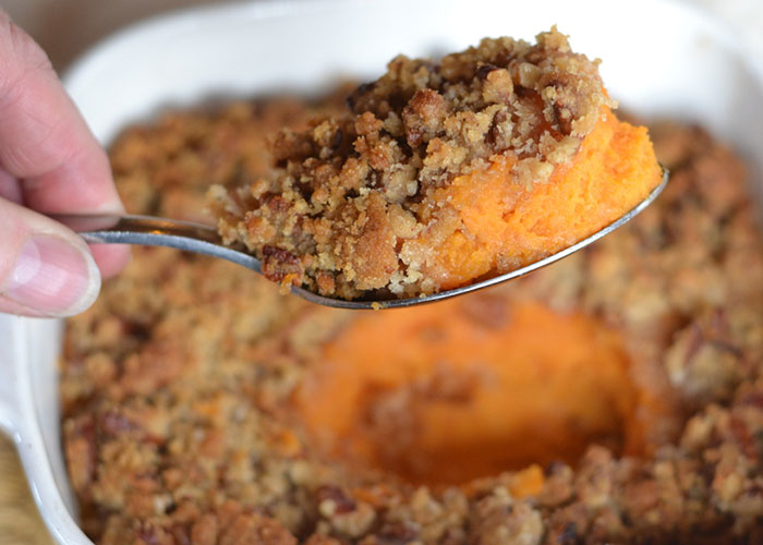Thanksgiving dish being served with a spoon, featuring a sweet potato casserole topped with a pecan crumble.