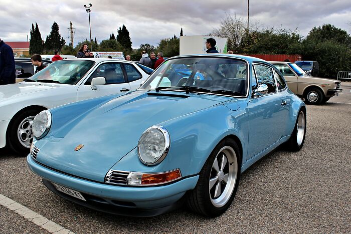 Classic blue sports car, a retiree's best gift to themselves, parked at a car show with other vintage vehicles in the background.