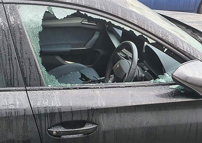 Broken car window seen while driving at night, shattered glass on a rainy vehicle.