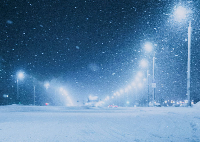 Snowy night driving scene with illuminated streetlights and snowfall.