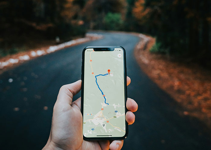 A hand holding a smartphone with GPS navigation on a dark, winding road at night.