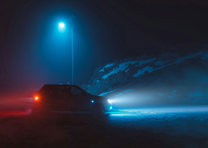 Car driving at night under a blue streetlight with fog creating a mysterious atmosphere.