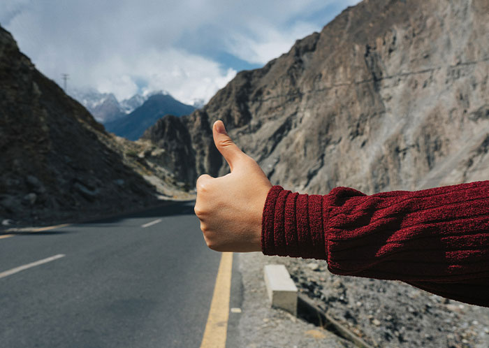 A hand in a red sleeve hitchhiking on a mountain road under a cloudy sky at night.