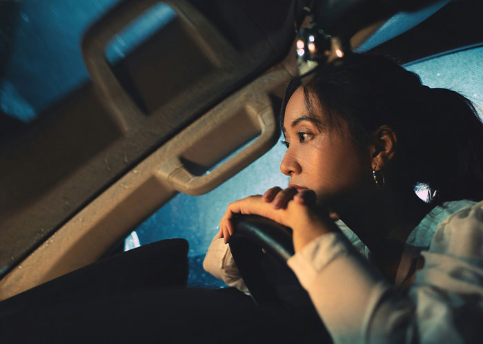 Woman driving at night, looking intently through a rain-specked windshield, curious about the unusual sights on the road.