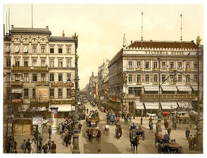Early 1900s street scene in color, showing historical architecture and horse-drawn carriages.