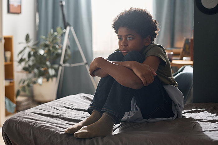 Child sitting on a bed looking pensive, contemplating family issues.