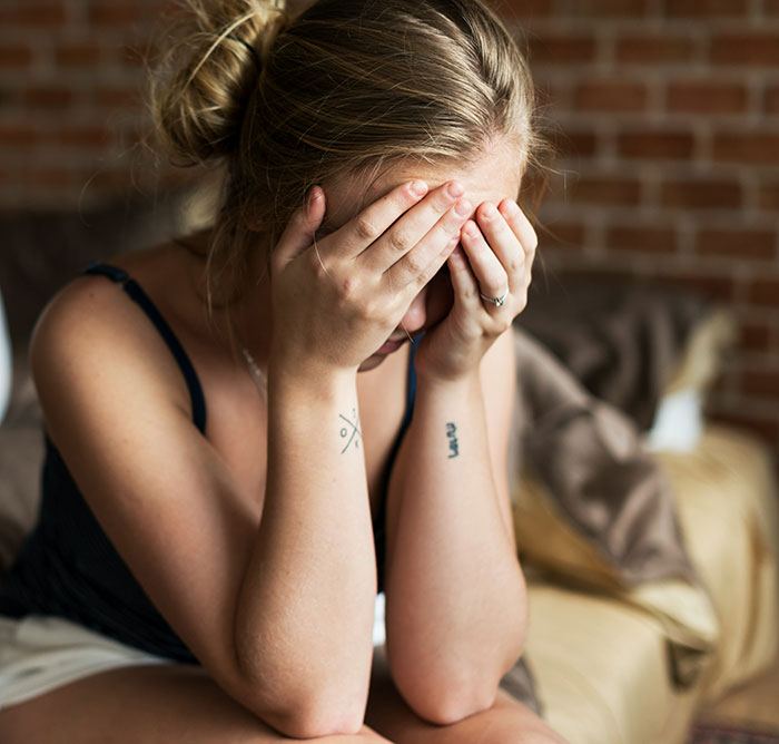 A woman sits on a bed, covering her face with her hands, expressing emotion related to family conflict and a wedding invitation.