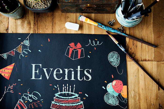 Events sign with birthday decorations, balloons, and paintbrushes on a wooden table.
