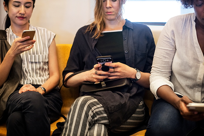 Three people sitting on a bench, each focused on their smartphones, unaware of their surroundings.