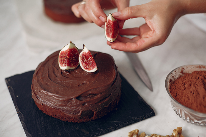 Person decorating chocolate cake with fresh figs on a slate plate, focusing on dessert presentation.