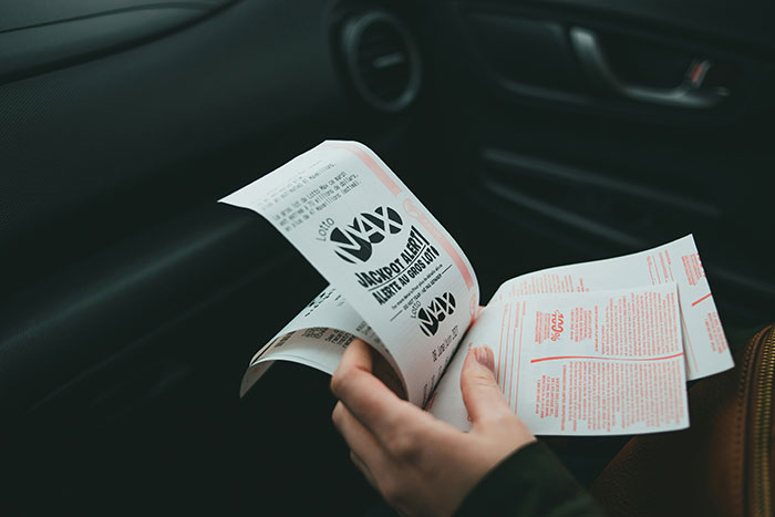 Person in a car holding lottery tickets, contemplating winnings. Person in a car holding lottery tickets, contemplating winnings.