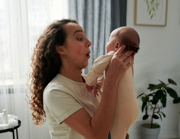 A woman playfully holds a baby in a cozy room, expressing surprise. A woman playfully holds a baby in a cozy room, expressing surprise.