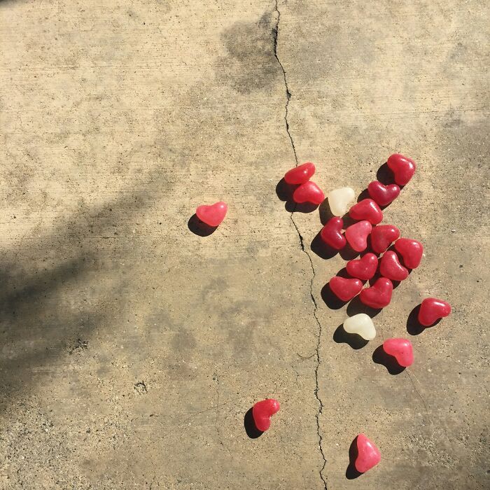 Red and white heart-shaped candies scattered on c*****d concrete.
