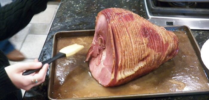 Hand glazing a large cooked ham on a baking tray, relating to strangest delivery stories.