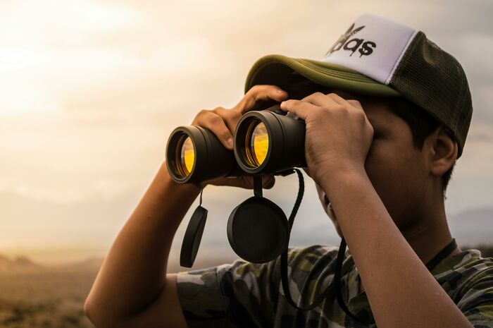 Person wearing a cap using binoculars, searching in the distance, related to strangest delivery stories.