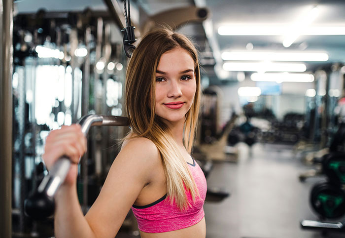 Woman in a gym lifting weights, representing fitness and strength, smiling confidently.