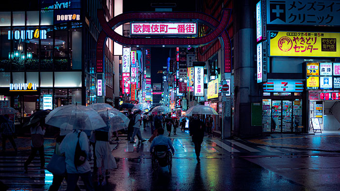 Nighttime street scene with umbrellas and neon signs, showcasing vibrant urban culture.