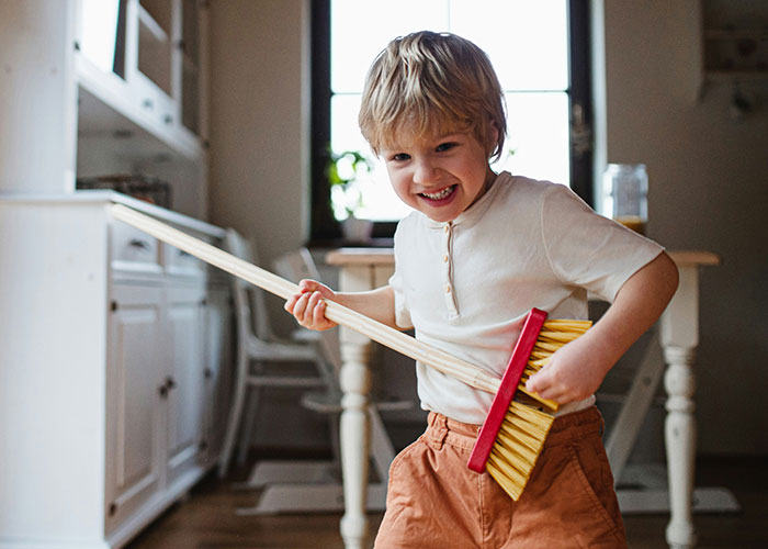 Young boy pretending to play guitar with a broom in a kitchen, illustrating times police were called for dumb reasons.