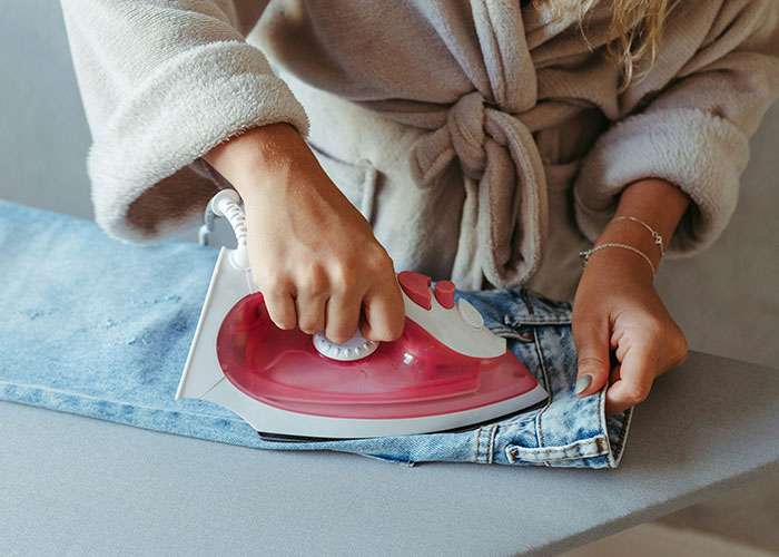 Person in a robe ironing jeans on an ironing board as police were called for the dumbest reasons involving everyday activities