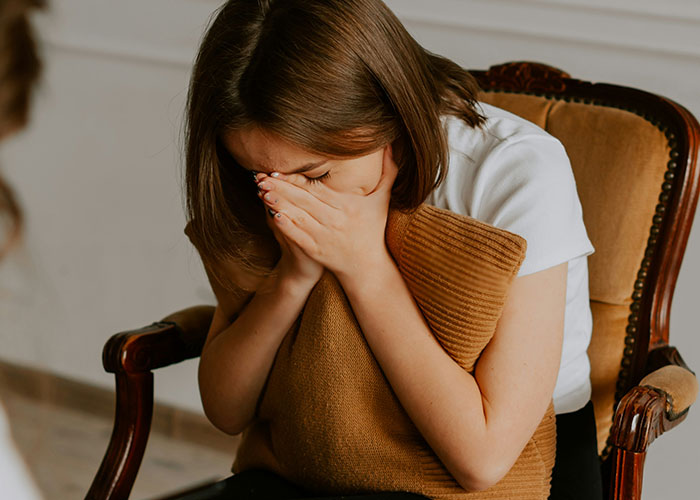 Young woman sitting on a chair, covering her face with hands, illustrating people called police for dumb reasons.