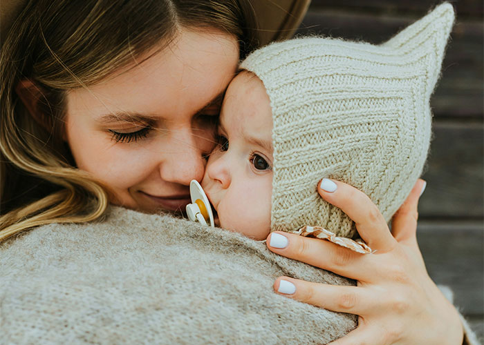 Mother tenderly hugging a baby dressed in a knitted hat, illustrating moments police were called on people for dumb reasons.