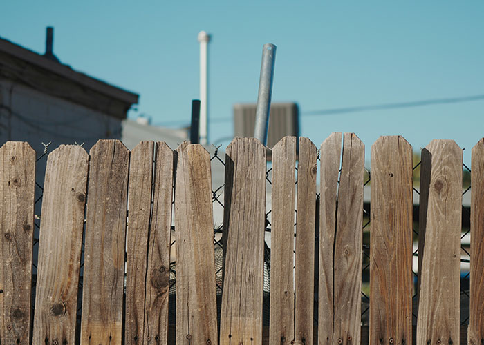 A weathered wooden fence in a residential area with pipes and rooftops visible, illustrating dumbest police calls.