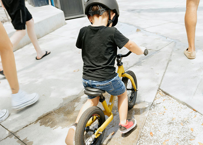 Young child wearing a helmet riding a yellow bike on the sidewalk with people walking nearby, illustrating dumbest reasons police called.