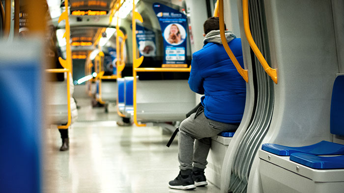 Man in blue jacket sitting alone on subway, facing away.
