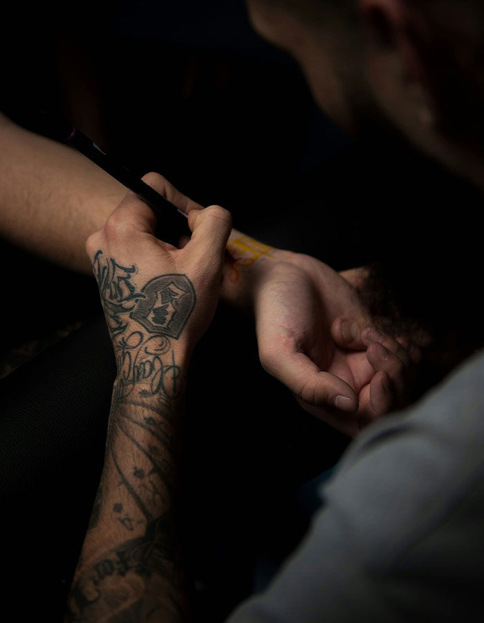 Person applying a temporary tattoo on someone's wrist in a dimly lit setting. Person applying a temporary tattoo on someone's wrist in a dimly lit setting.