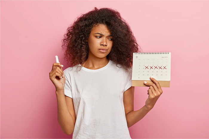 Woman holding a calendar marked with Xs, representing teacher clocking periods, looks puzzled against a pink background. Woman holding a calendar marked with Xs, representing teacher clocking periods, looks puzzled against a pink background.