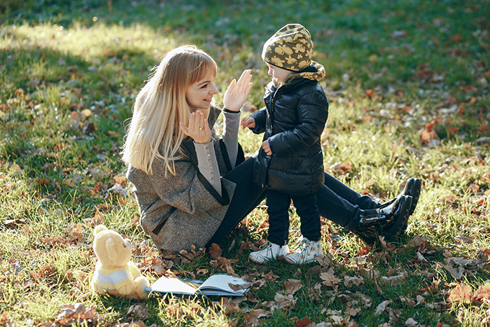 Woman sitting on grass playing with a toddler, surrounded by autumn leaves. Woman sitting on grass playing with a toddler, surrounded by autumn leaves.