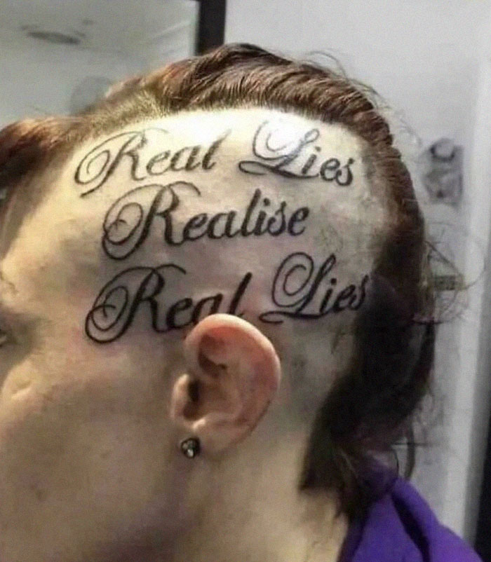 Person with head tattoo reading "Real Lies Realise Real Lies" in stylized script.
