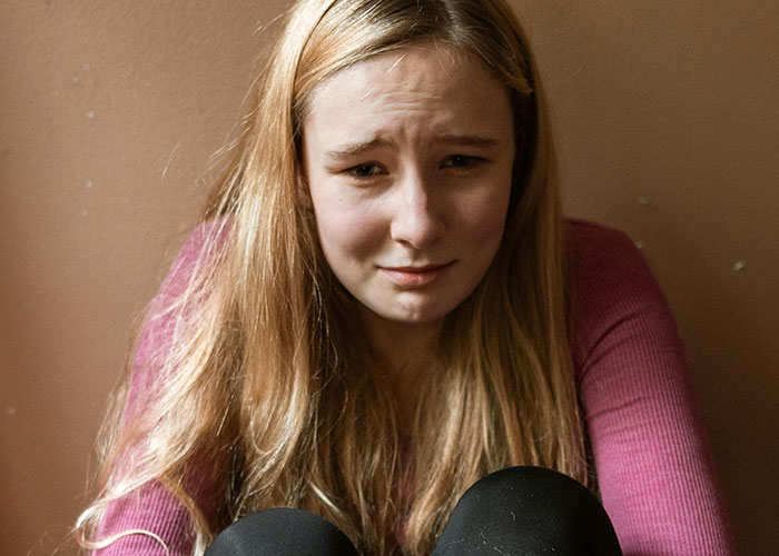 Young woman in a pink sweater looking distressed, sitting against a wall. Thanksgiving turn of events.