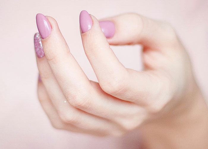 A hand with painted pink and glitter nails, capturing a quirky Thanksgiving moment.