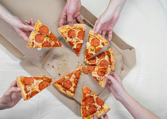 Hands grabbing slices of pepperoni pizza from a box, symbolizing a funny Thanksgiving meal twist.