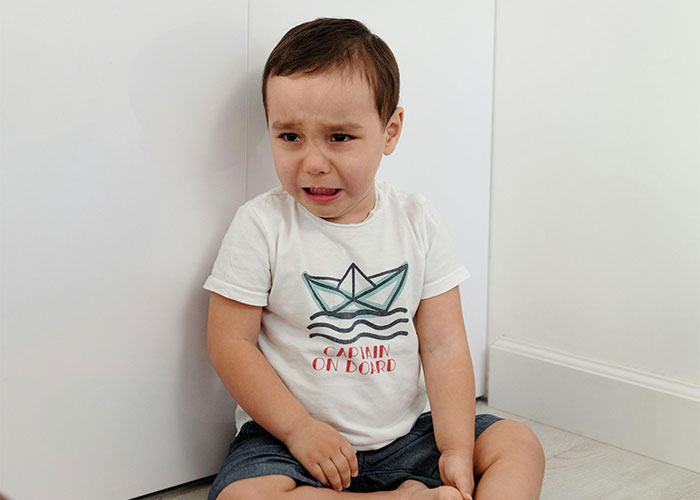 Crying toddler sitting on the floor during a Thanksgiving moment, wearing a t-shirt with a boat graphic.