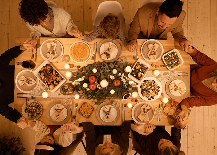 Thanksgiving dinner with family holding hands around a festive table, candles lit, and various dishes served.