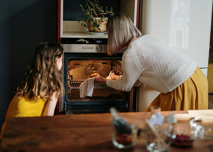 Woman and child checking turkey in oven for Thanksgiving meal preparation.