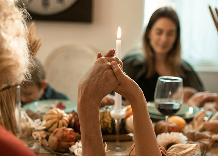 Thanksgiving gathering with hands held in prayer over a festive dinner table.