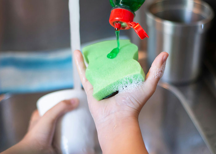 Thanksgiving gone wrong: hand with sponge and soap under running water in kitchen setting.