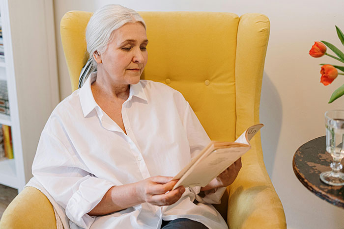 Elderly woman in a yellow chair, reading a menu, linked to a family Thanksgiving dinner story involving a hidden cake and backup pie.