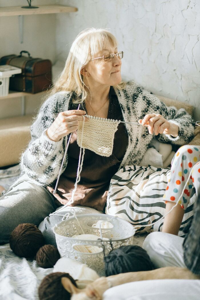 Person knitting on a couch with yarn and cozy decor, showcasing a relaxing moment.