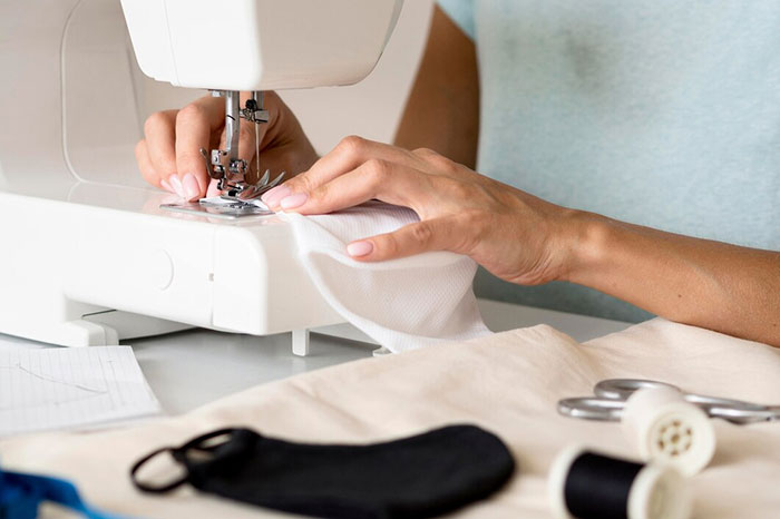 Adult using a sewing machine, a childhood denied item, while crafting fabric pieces with scissors and thread nearby.