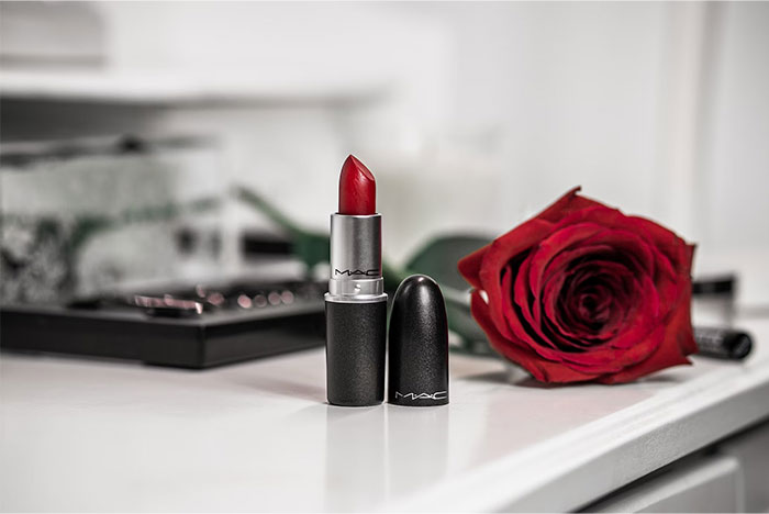 Red lipstick and rose on a table, representing things people bought as adults after being denied them in childhood.