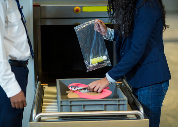 Person at airport security with interesting items in a tray, inspecting liquids in a plastic bag near the scanner.