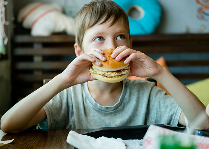 Child eating a burger at a table, reflecting on intriguing facts from the TIL community.
